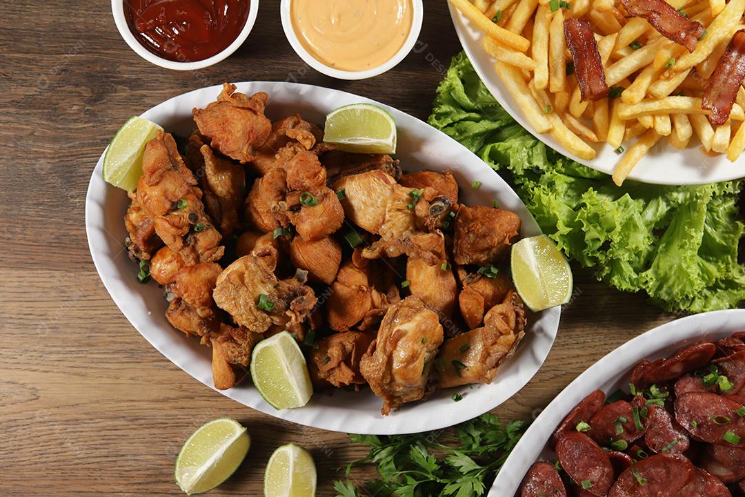 Porção de linguiça calabresa com limão, batata frita, bacon e frango frito. Alface, batata, cebolinha, ketchup e maionese.