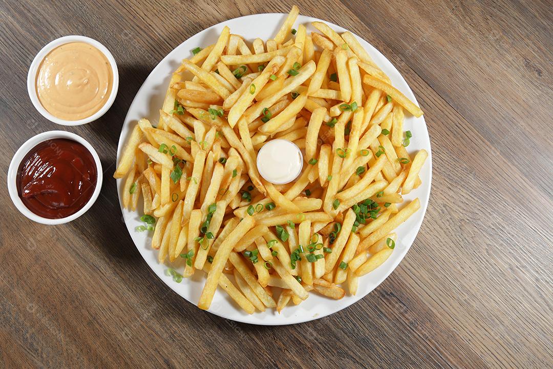 Porção de batatas fritas. Alface, batata, cebolinha, tomate, ketchup e maionese.