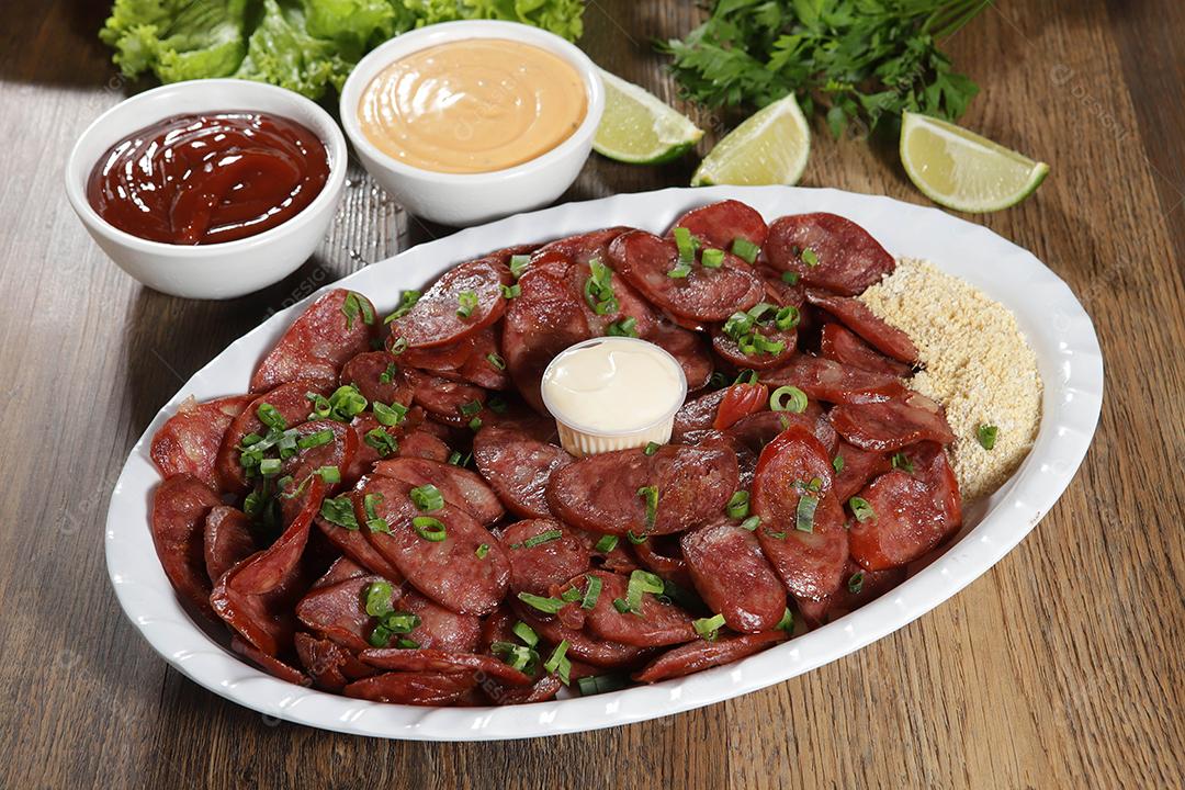 Porção de linguiça calabresa com limão. Alface, cebolinha, ketchup e maionese.