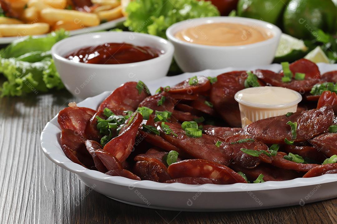 Porção de linguiça calabresa com limão. Alface, cebolinha, ketchup e maionese.