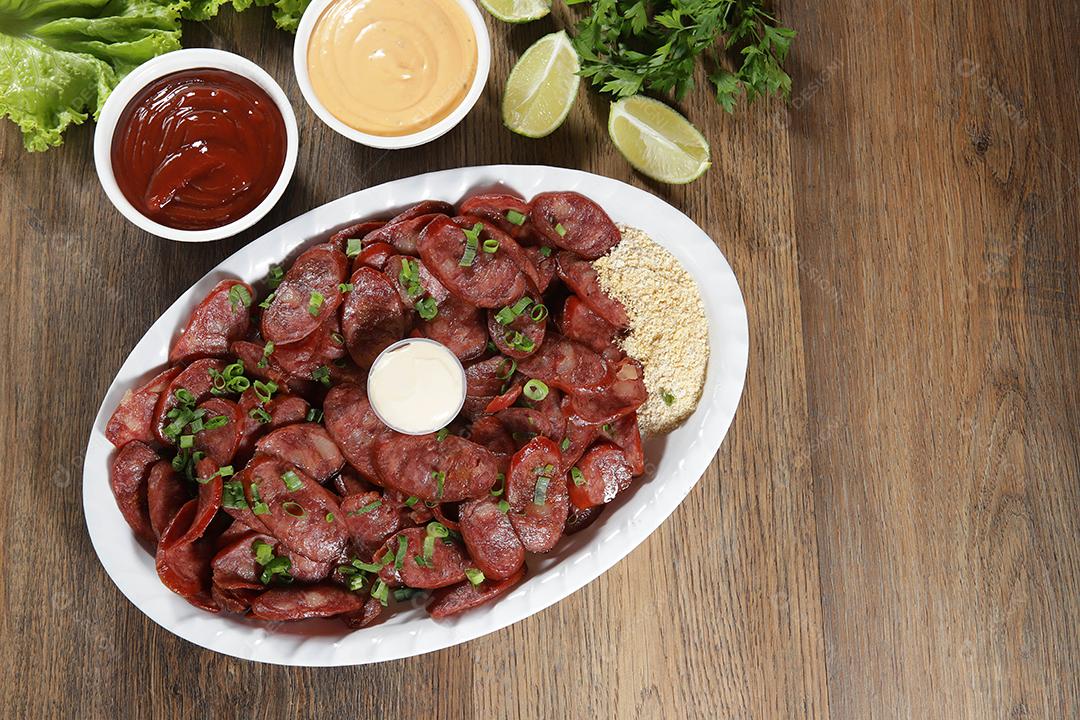 Porção de linguiça calabresa com limão. Alface, cebolinha, ketchup e maionese.