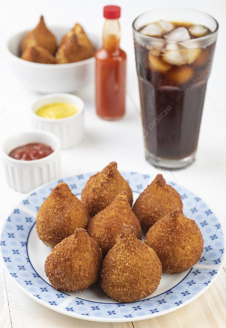 Coxinha de lanche típico brasileiro em um prato com copo de refrigerante.