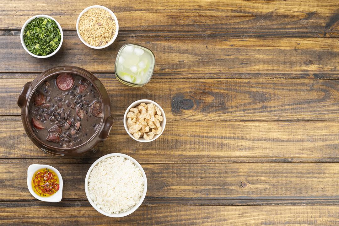 Tradicional feijoada brasileira com farinha de mandioca, couve, caipirinha, arroz, torresmo e espaço para cópia.