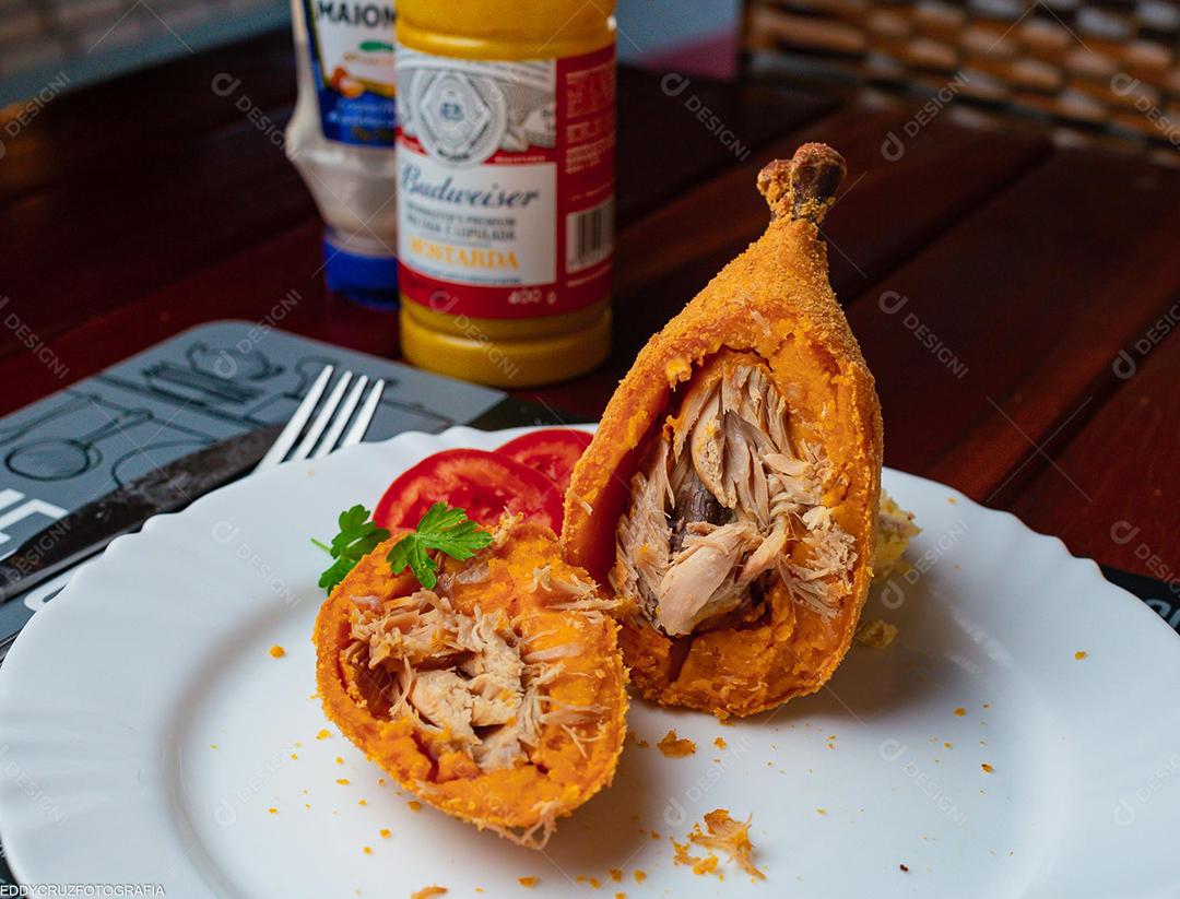 Coxinha ao meio sobre prato branco em mesa madeira