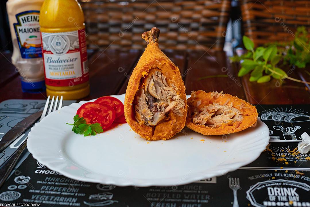 Coxinha ao meio sobre prato branco em mesa madeira