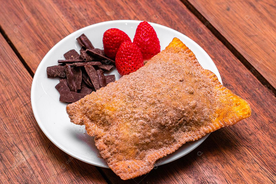 Pastel de vento servido em prato branco com morango e chocolate