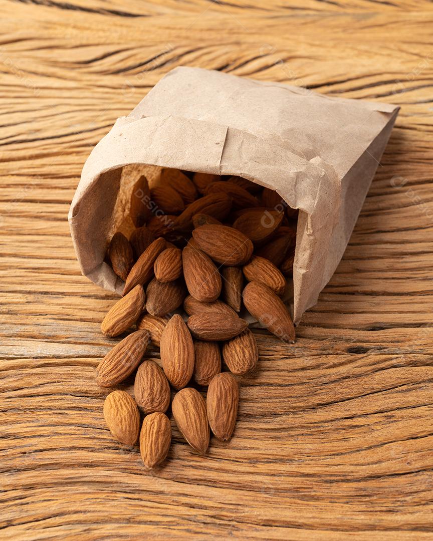 Amêndoas em um saco de papel sobre a mesa de madeira.