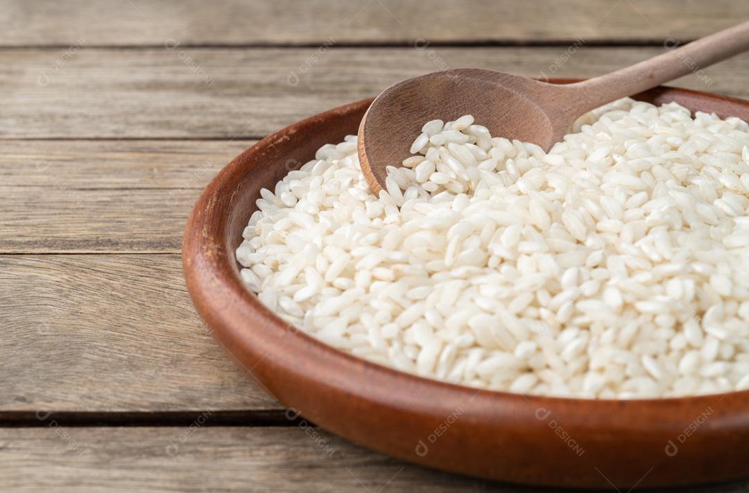 Foco estreito, arroz de risoto de carnaroli cru em um prato sobre madeira