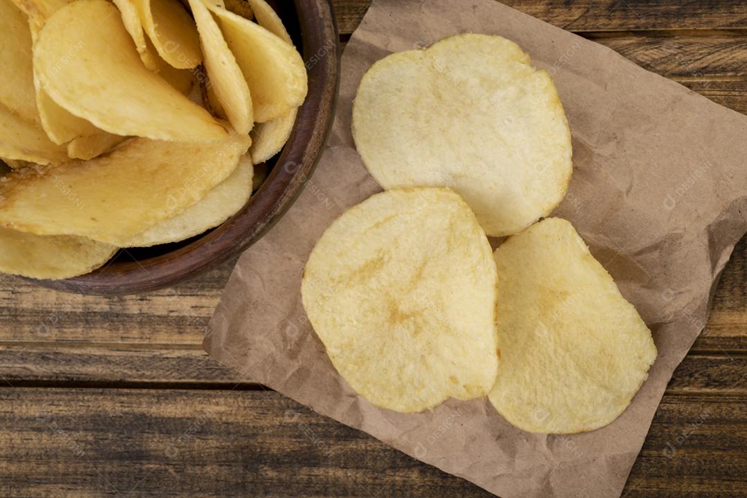 Batatas fritas em uma tigela e em um pedaço de papel sobre a mesa de madeira
