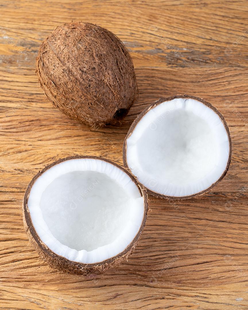 Coco e meia fruta rachada sobre a mesa de madeira.