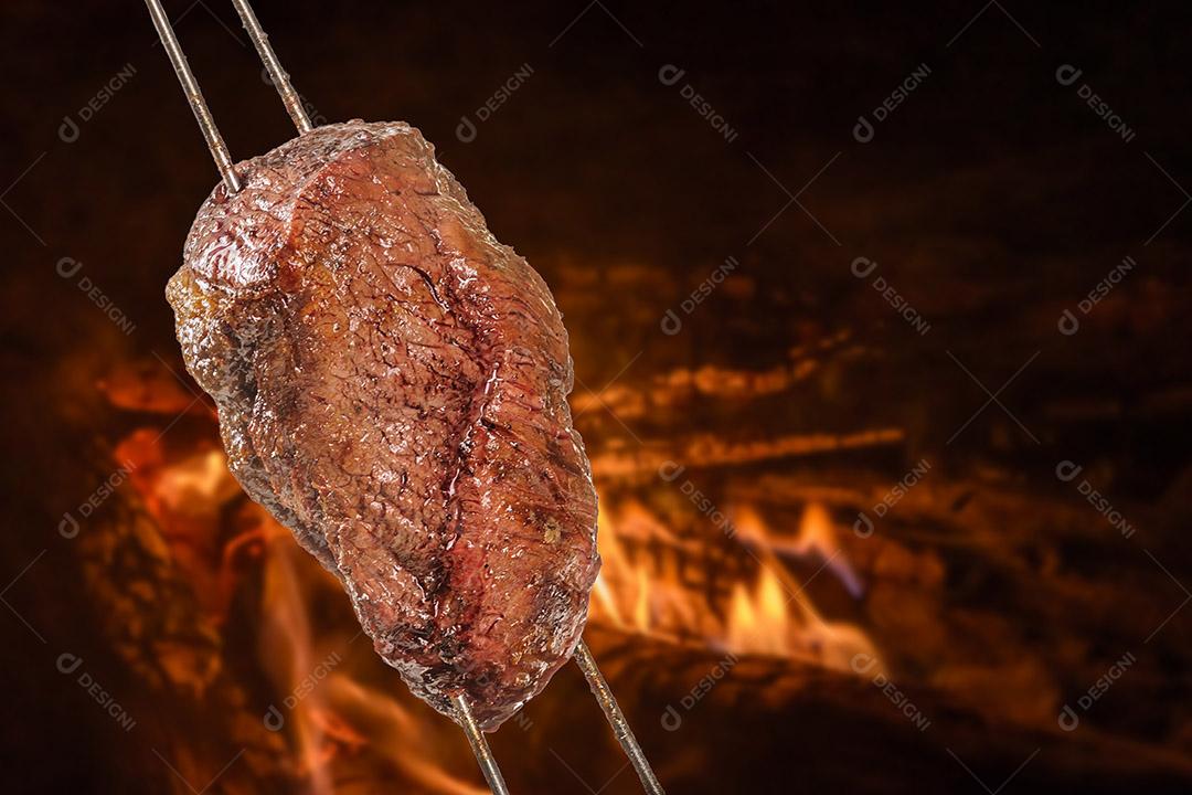 Churrasco de picanha assada com fogo desfocado ao fundo. Também chamado de churrasquinho.