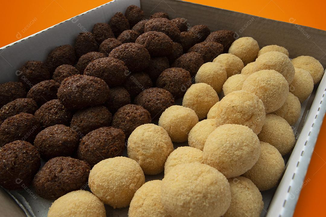 Uma caixa de croquetes fritos e aperitivos para entrega. Coxinha de lanche brasileiro em fundo amarelo e laranja.