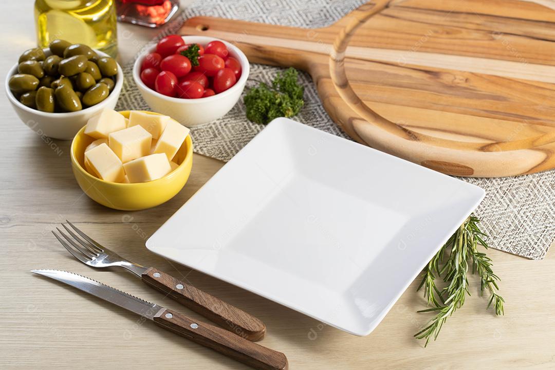 Prato quadrado branco vazio em cima da mesa com queijo, azeitonas e tomate cereja