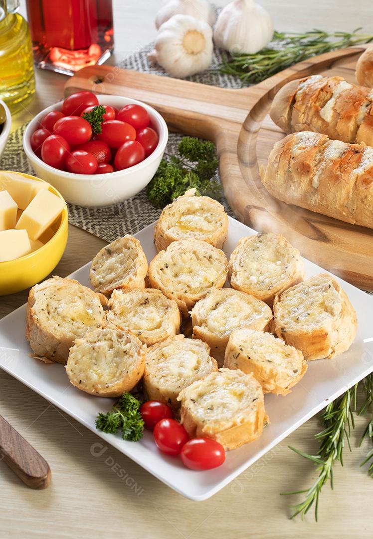 Pão de alho em prato quadrado branco em cima da mesa com queijo, alecrim, azeitonas e tomate cereja