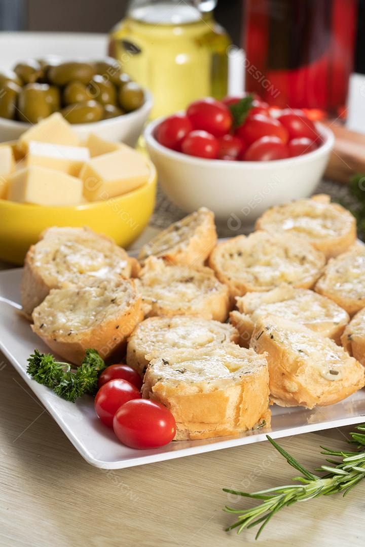 Pão de alho em prato quadrado branco em cima da mesa com queijo, alecrim, azeitonas e tomate cereja