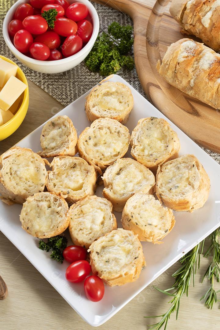 Pão de alho em prato quadrado branco em cima da mesa com queijo, alecrim, azeitonas e tomate cereja
