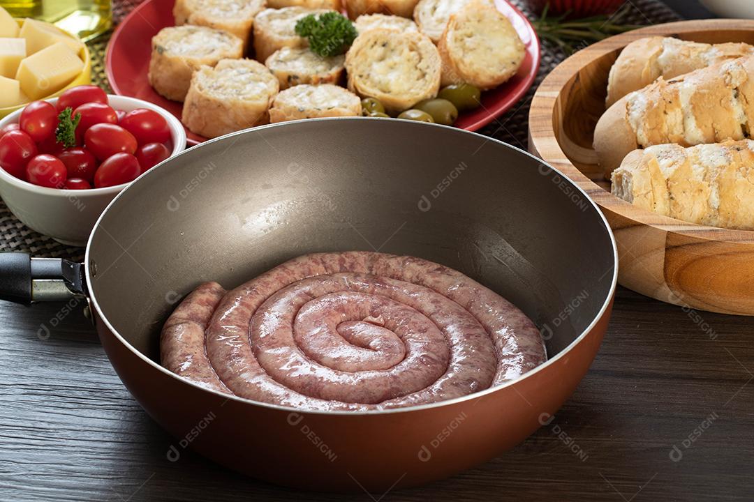 Pão de salsicha e alho em um prato vermelho na mesa de churrasco com aperitivos, queijo, alecrim, azeitonas e tomate cereja