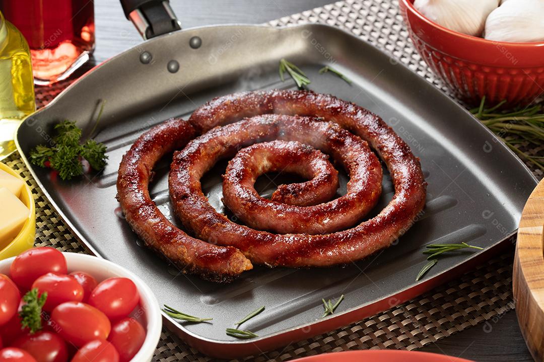 Pão de salsicha e alho em um prato vermelho na mesa de churrasco com aperitivos, queijo, alecrim, azeitonas e tomate cereja