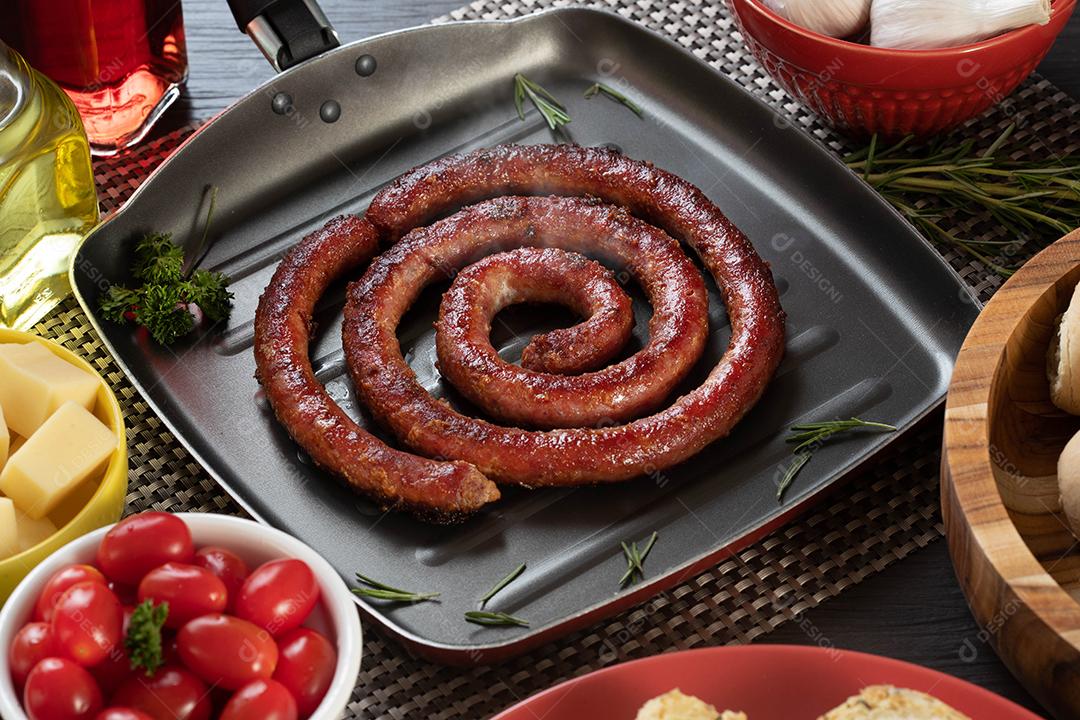 Pão de salsicha e alho em um prato vermelho na mesa de churrasco com aperitivos, queijo, alecrim, azeitonas e tomate cereja