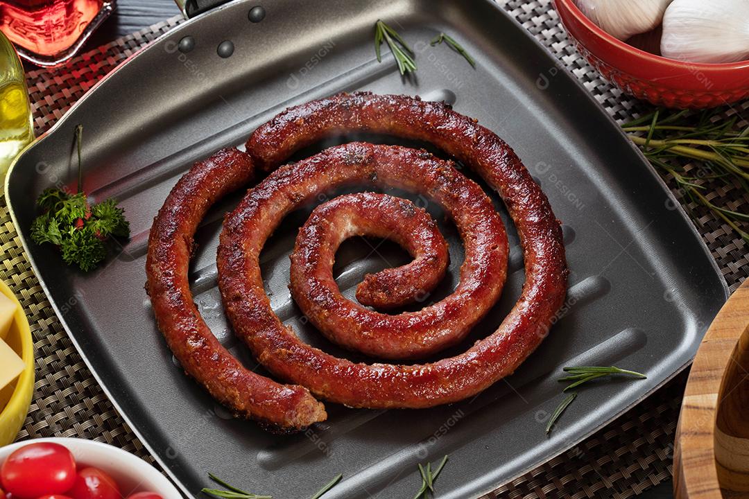 Pão de salsicha e alho em um prato vermelho na mesa de churrasco com aperitivos, queijo, alecrim, azeitonas e tomate cereja