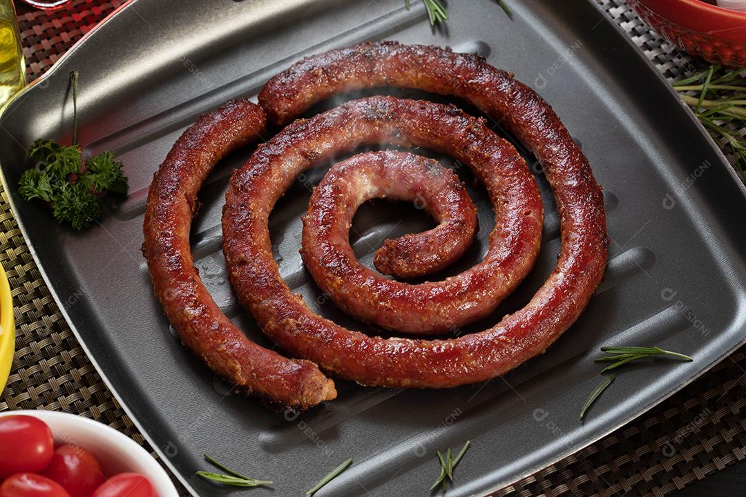 Pão de salsicha e alho em um prato vermelho na mesa de churrasco com aperitivos, queijo, alecrim, azeitonas e tomate cereja