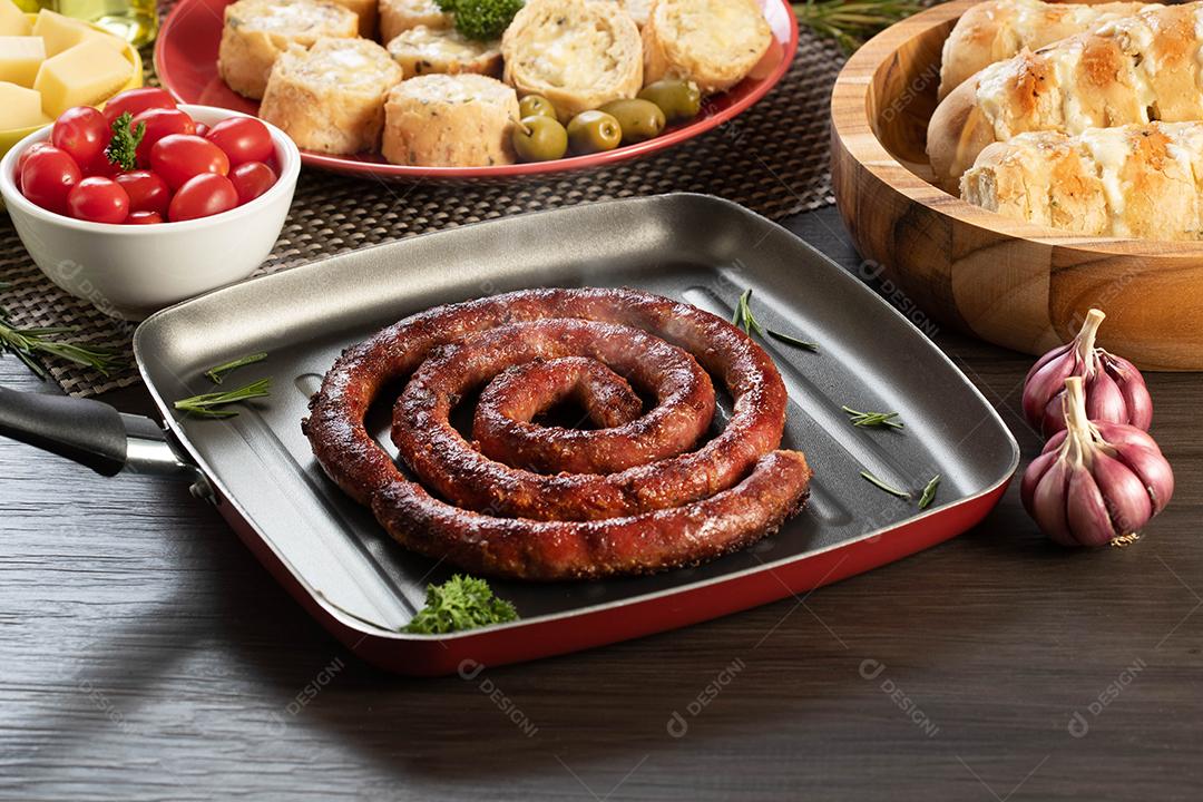 Pão de salsicha e alho em um prato vermelho na mesa de churrasco com aperitivos, queijo, alecrim, azeitonas e tomate cereja