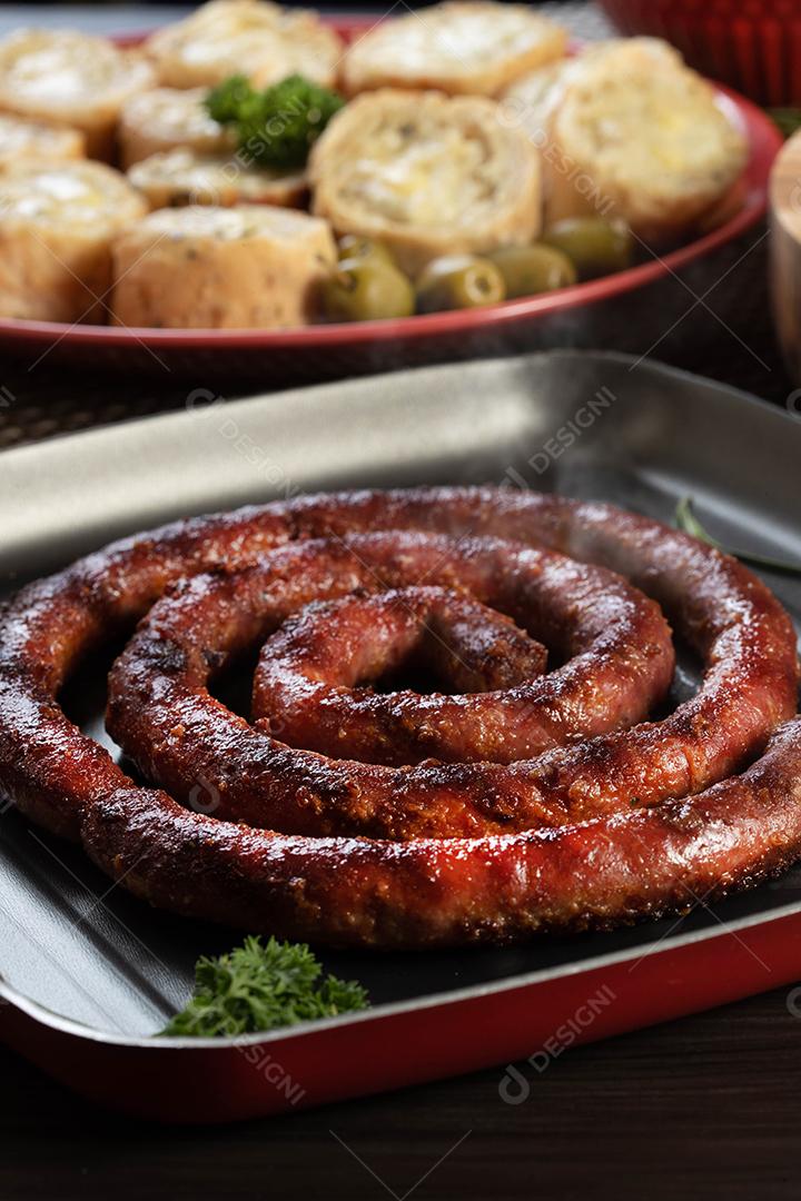 Pão de salsicha e alho em um prato vermelho na mesa de churrasco com aperitivos, queijo, alecrim, azeitonas e tomate cereja