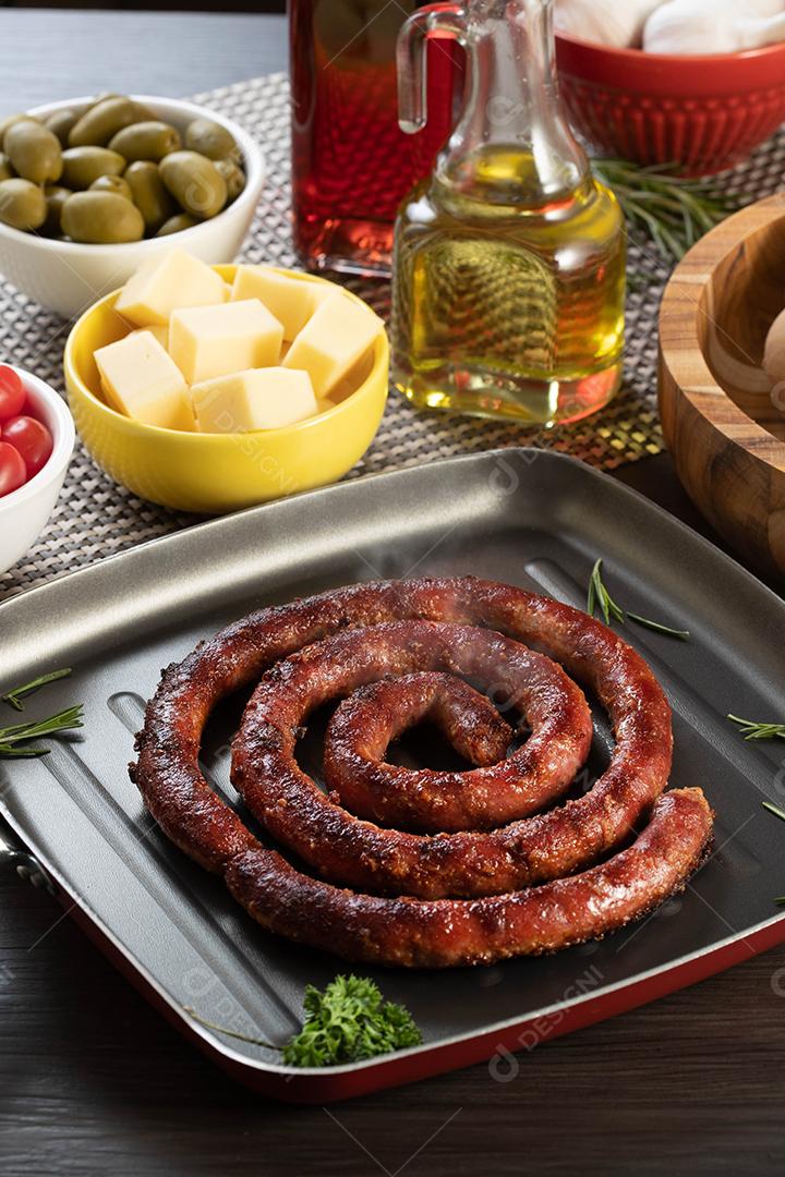 Pão de salsicha e alho em um prato vermelho na mesa de churrasco com aperitivos, queijo, alecrim, azeitonas e tomate cereja