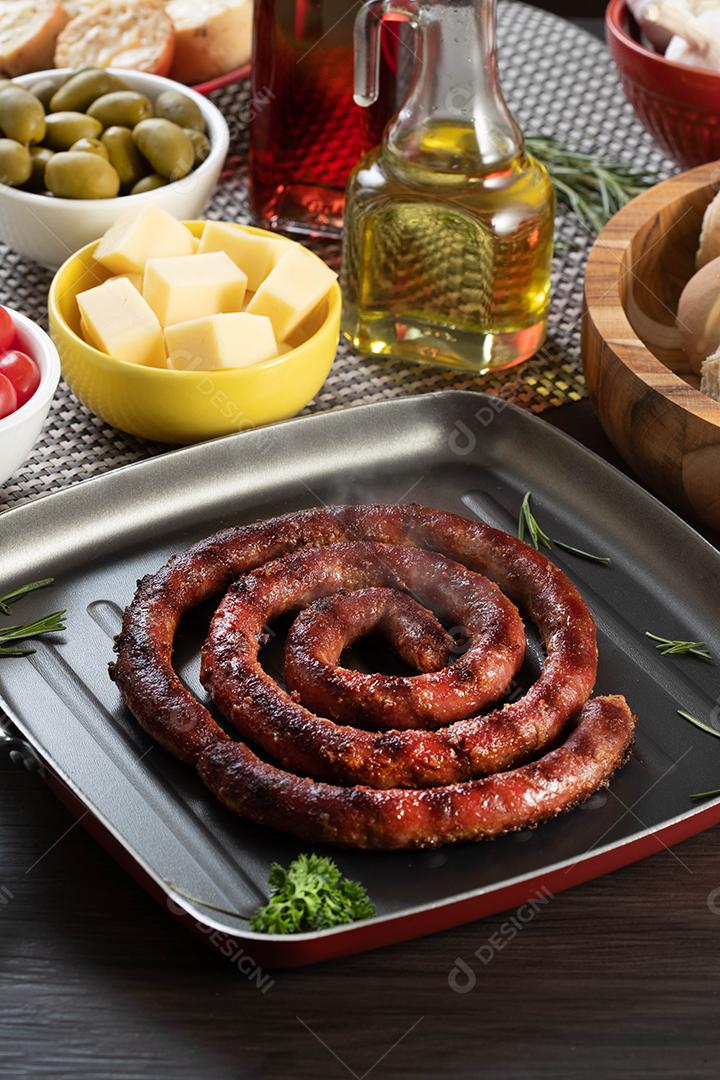 Pão de salsicha e alho em um prato vermelho na mesa de churrasco com aperitivos, queijo, alecrim, azeitonas e tomate cereja