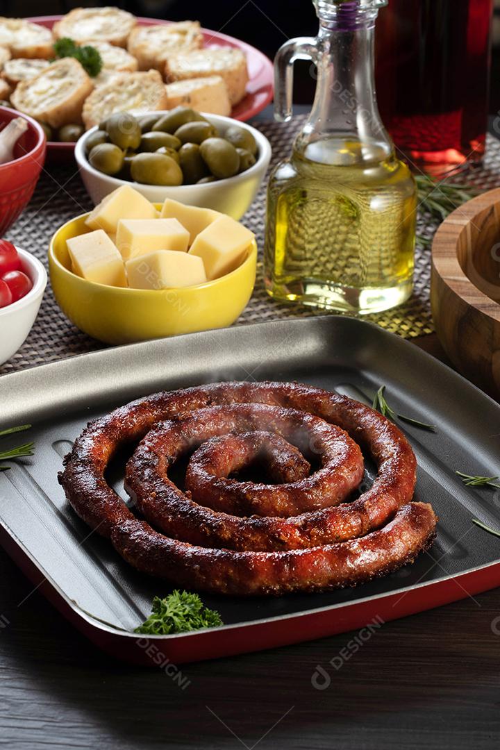 Pão de salsicha e alho em um prato vermelho na mesa de churrasco com aperitivos, queijo, alecrim, azeitonas e tomate cereja