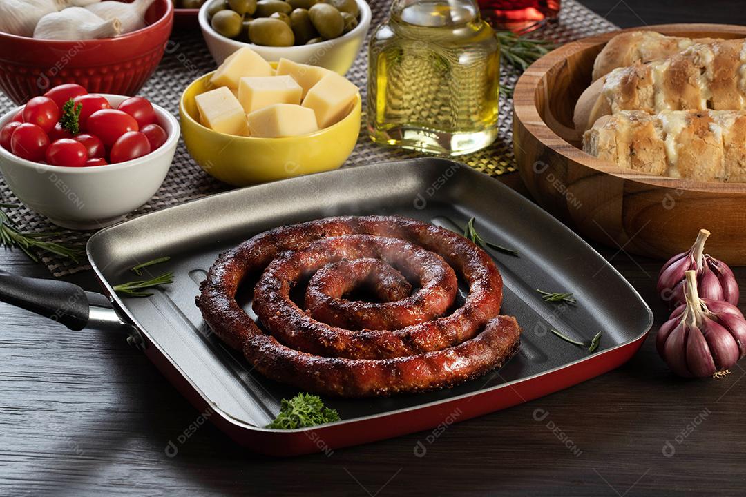 Pão de salsicha e alho em um prato vermelho na mesa de churrasco com aperitivos, queijo, alecrim, azeitonas e tomate cereja