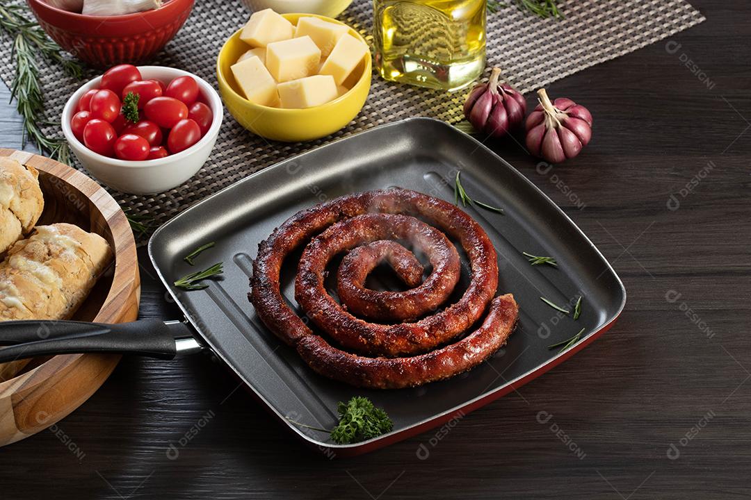 Pão de salsicha e alho em um prato vermelho na mesa de churrasco com aperitivos, queijo, alecrim, azeitonas e tomate cereja