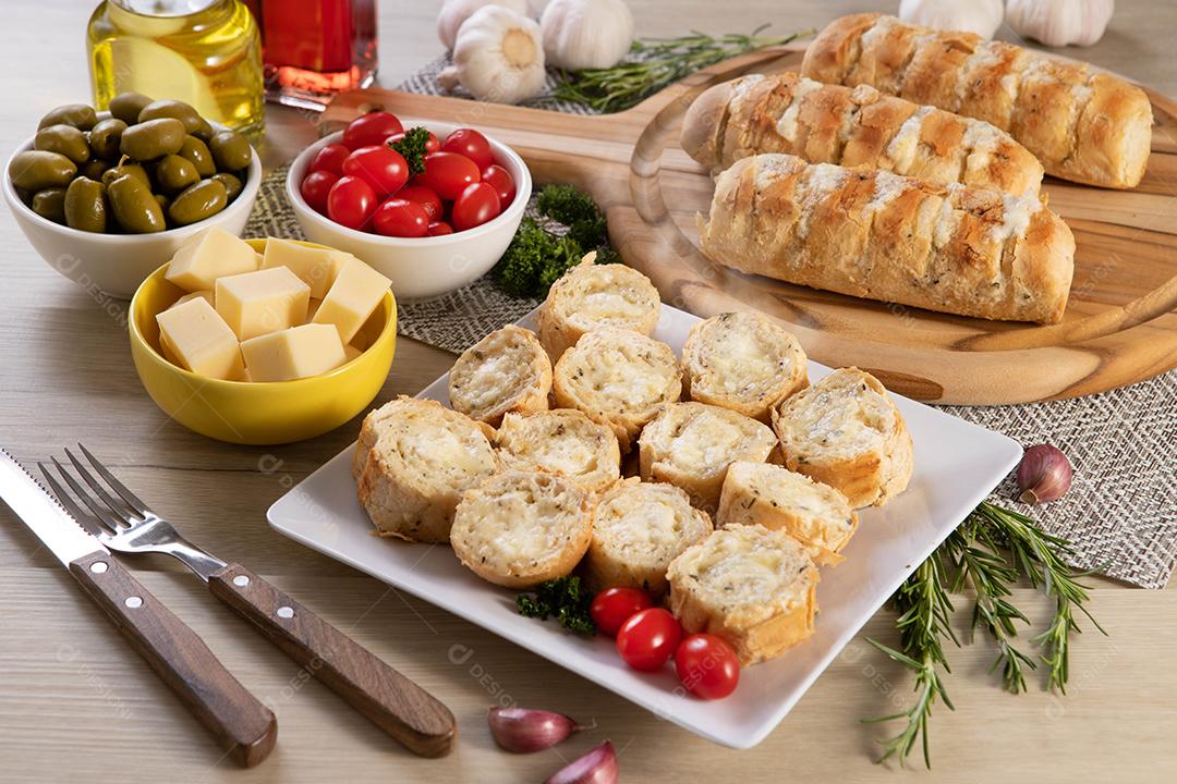 Pão de alho em prato quadrado branco em cima da mesa com queijo, alecrim, azeitonas e tomate cereja