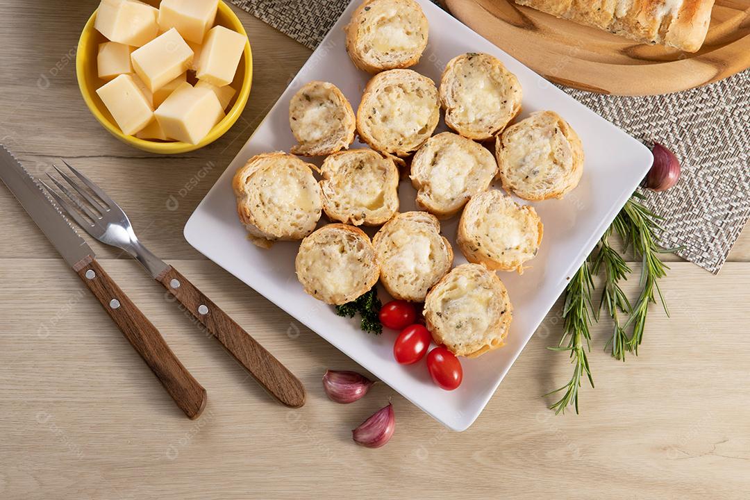 Pão de alho em prato quadrado branco em cima da mesa com queijo, alecrim, azeitonas e tomate cereja