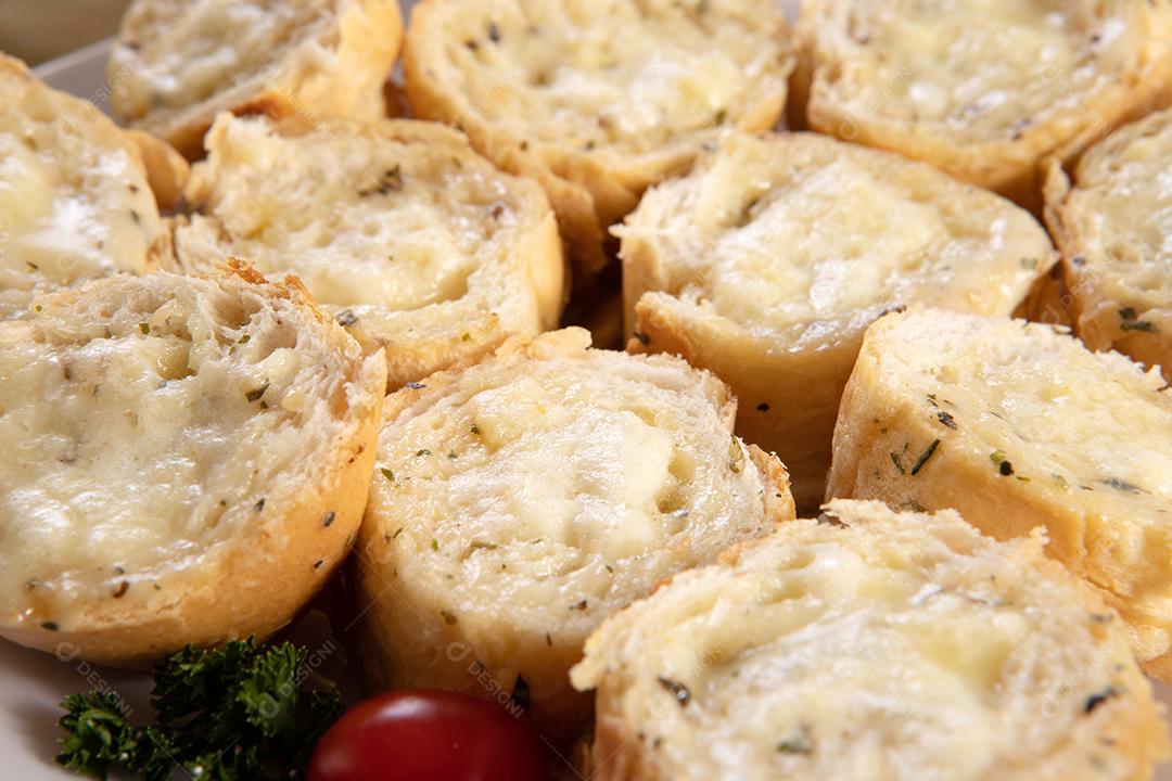 Pão de alho em prato quadrado branco em cima da mesa com queijo, alecrim, azeitonas e tomate cereja