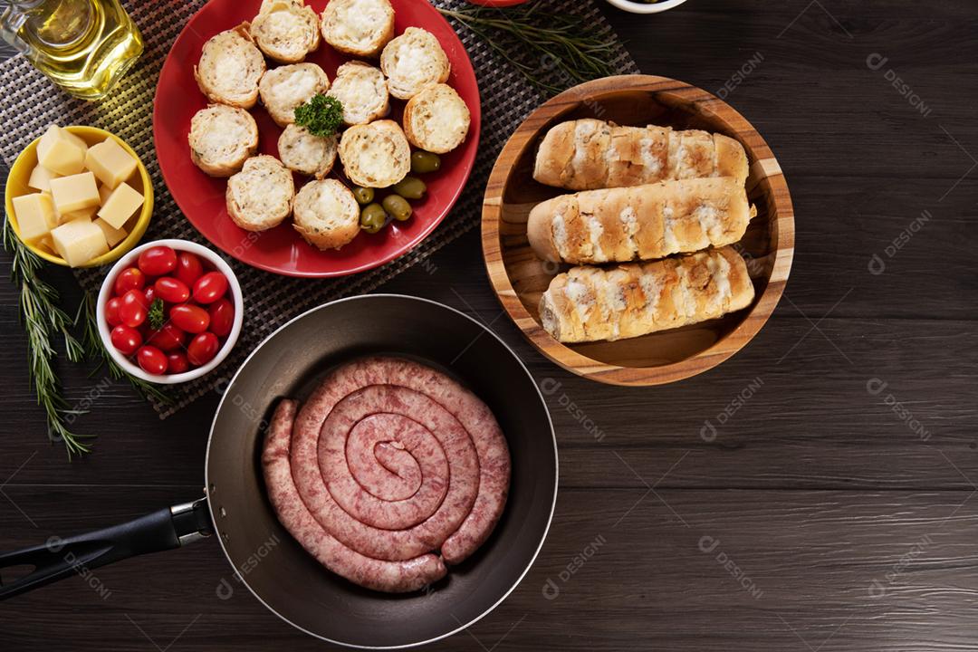 Linguiça crua com pão de salsicha e alho em um prato vermelho na mesa de churrasco wi