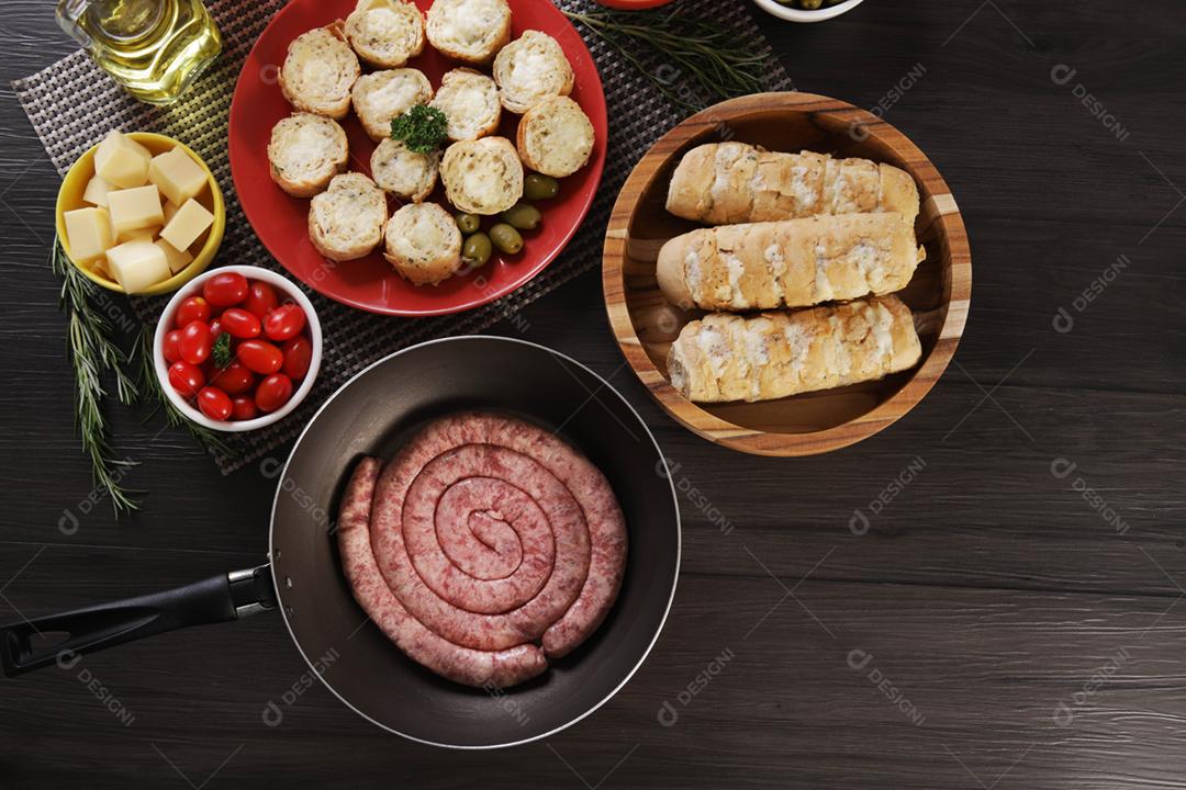 Linguiça crua com pão de salsicha e alho em um prato vermelho na mesa de churrasco wi