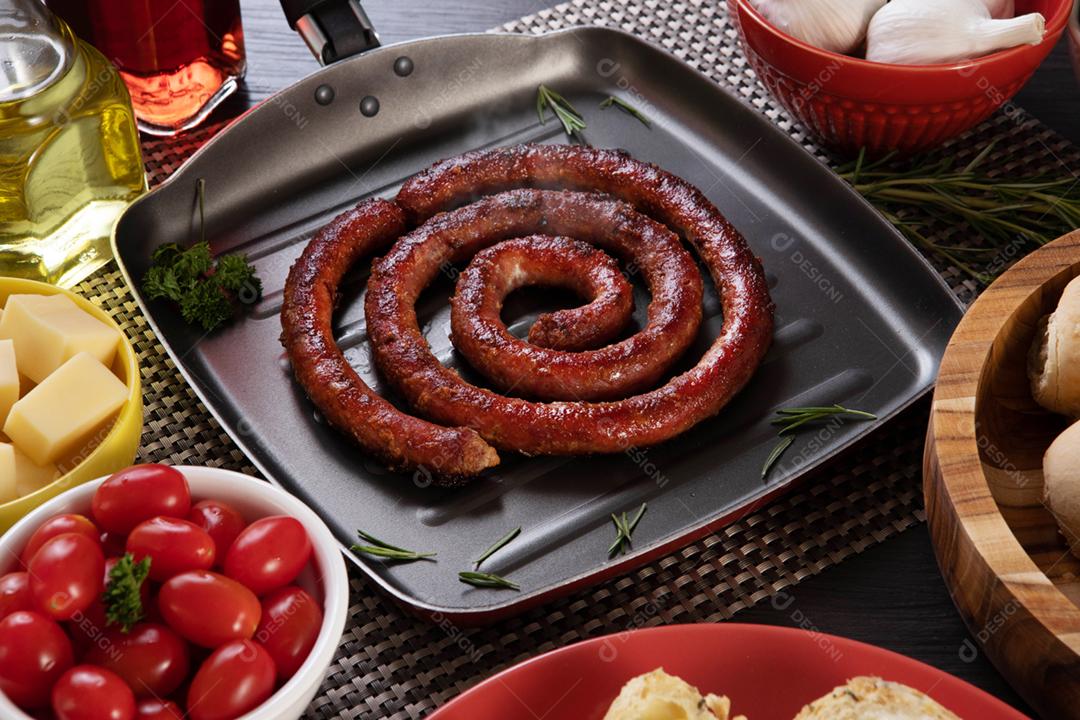 Linguiça assada com pão de salsicha e alho em um prato vermelho na mesa de churrasco wi