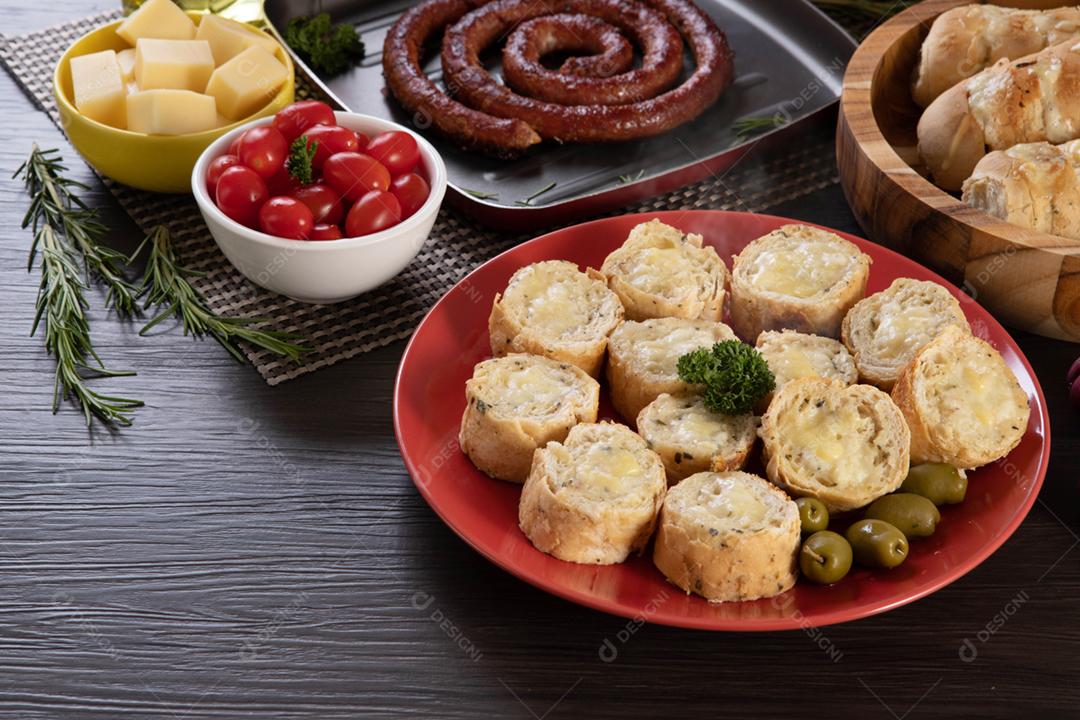 Pão de alho em um prato vermelho na mesa de churrasco com salsicha,