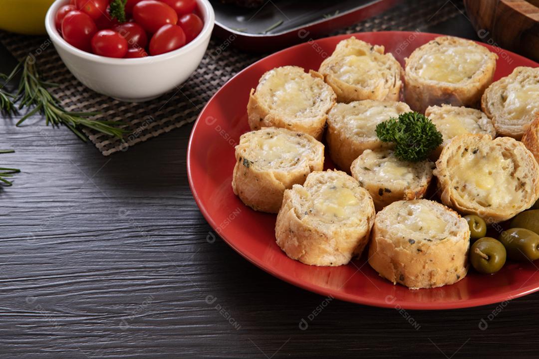 Pão de alho em um prato vermelho na mesa de churrasco com salsicha,