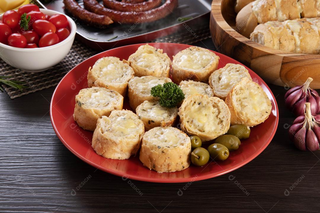 Pão de alho em um prato vermelho na mesa de churrasco com salsicha,