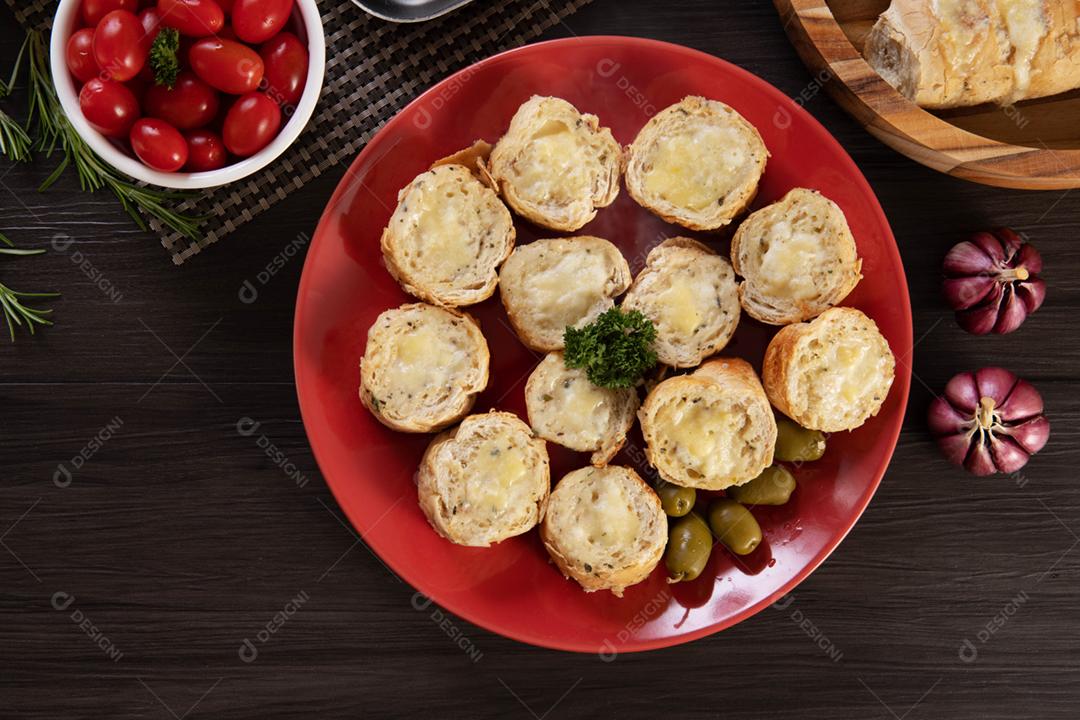 Pão de alho em um prato vermelho na mesa de churrasco com salsicha,