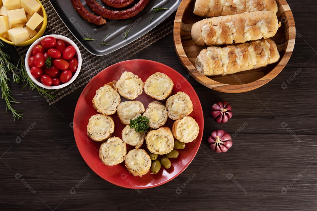 Pão de alho em um prato vermelho na mesa de churrasco com salsicha,