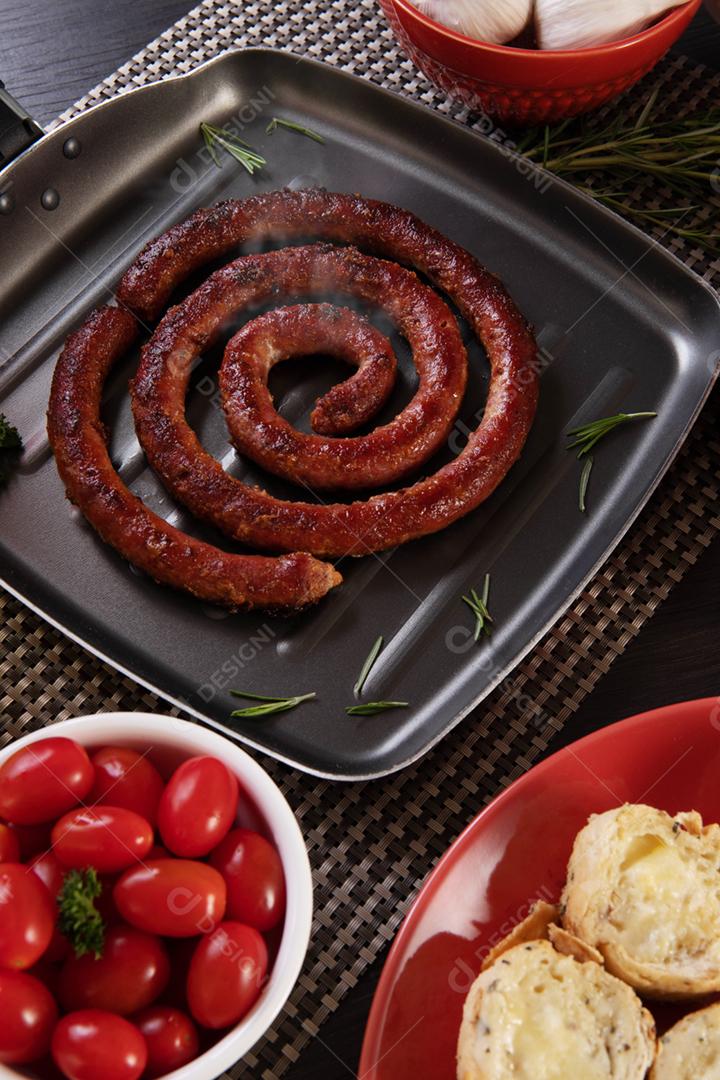 Linguiça assada com pão de salsicha e alho em um prato vermelho na mesa de churrasco wi
