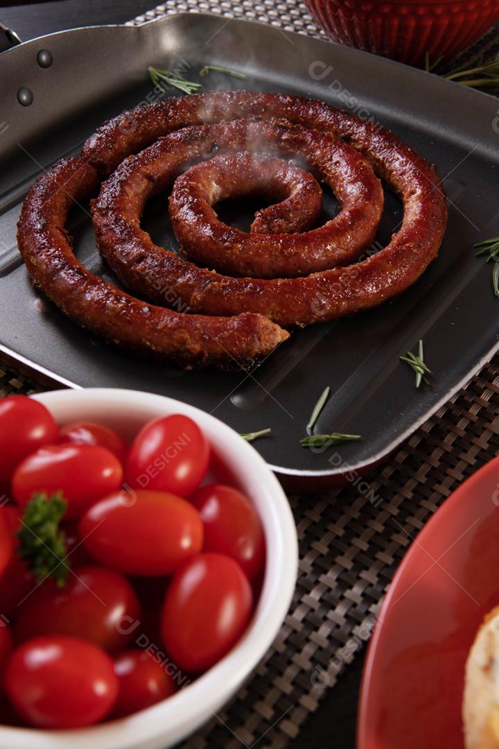 Linguiça assada com pão de salsicha e alho em um prato vermelho na mesa de churrasco wi