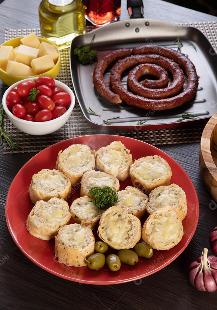 Pão de alho em um prato vermelho na mesa de churrasco com salsicha,
