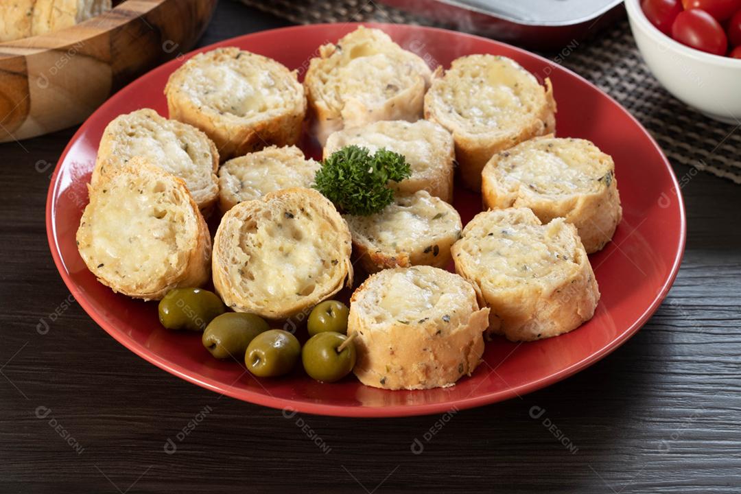 Pão de alho em um prato vermelho na mesa de churrasco com salsicha,