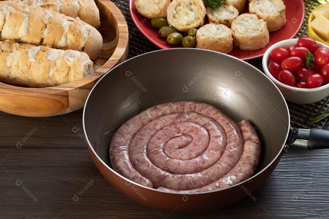 Linguiça crua com pão de salsicha e alho em um prato vermelho na mesa de churrasco wi