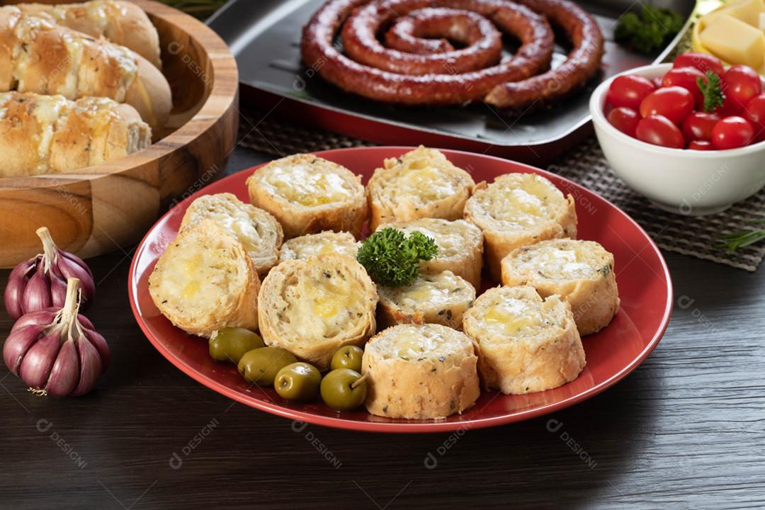 Pão de alho em um prato vermelho na mesa de churrasco com salsicha,
