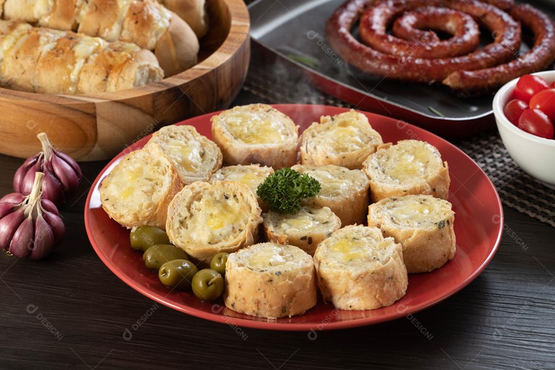 Pão de alho em um prato vermelho na mesa de churrasco com salsicha,